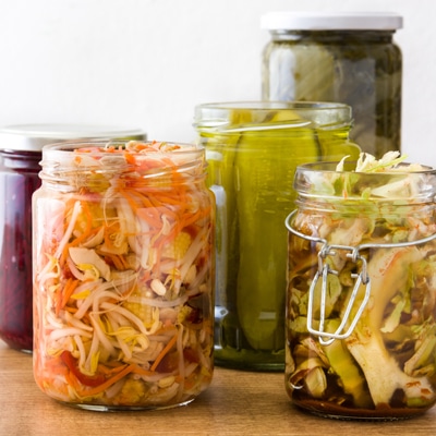 Fermented preserved vegetables in jar on wooden table.